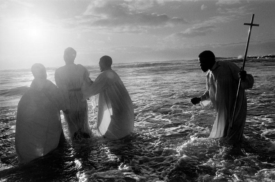 هنگام طلوع آفتاب، کشیشان کلیسای صهیون، افراد تازه ایمان آورده را در دریا غسل تعمید می‌دهند. کیپ تاون، آفریقای جنوبی، ۱۹۹۹.