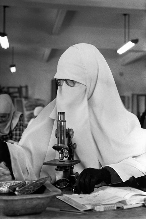یک دانشجوی دختر، با پوشش کامل اسلامی، در حال کار با یک میکروسکوپ در دپارتمان بیولوژی دانشگاه قاهره. قاهره، مصر، ۱۹۸۷.